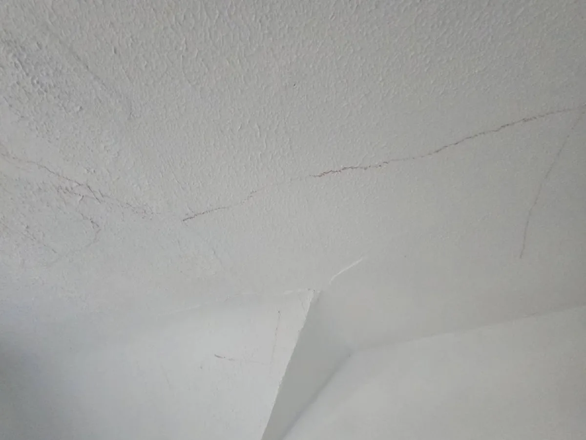 A textured ceiling and wall corner with visible cracks