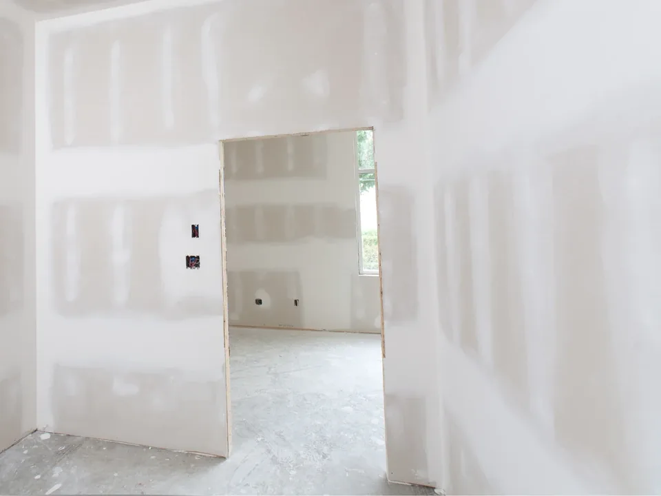 A room with drywall seams taped and covered in joint compound, with a doorway to another room