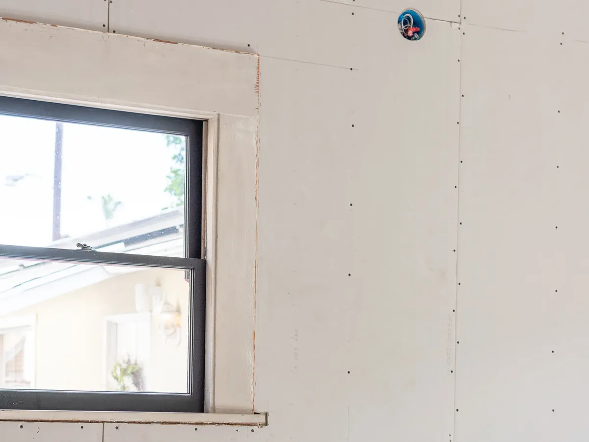An interior room with drywall sheets fastened to the walls around a window