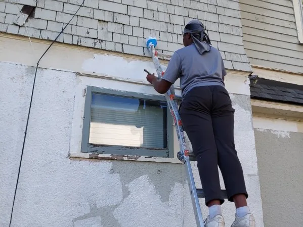 A painter on a ladder working on an exterior wall with patched and primed areas
