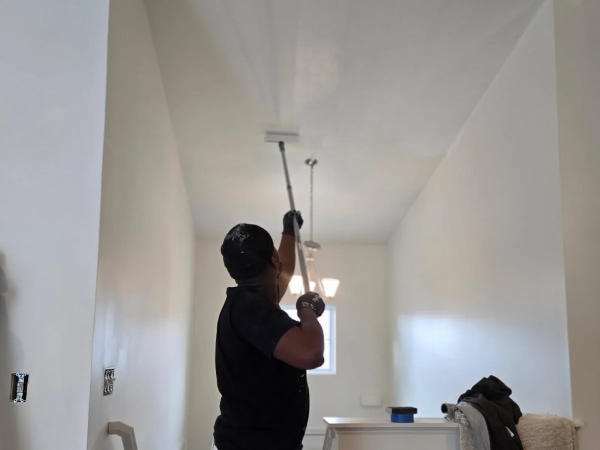 A painter rolling the ceiling of a bright hallway with white walls